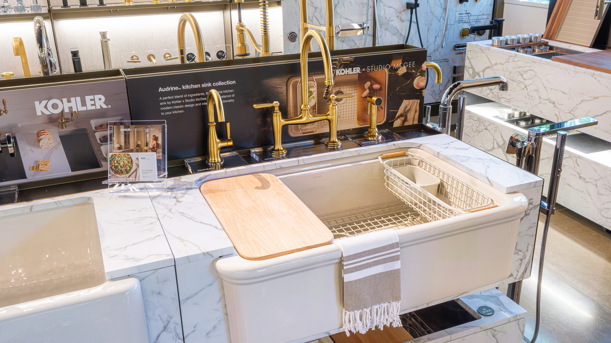 Showroom Kohler kitchen display with Studio McGee Audrine workstation and accessories, cutting board, strainer, bottom grid